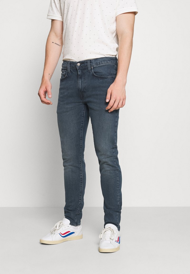 Mörkblå smala jeans i denim, med en klassisk femficksdesign och knappstängning, tillsammans med vita sneakers.