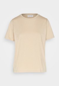 Béžové tričko s krátkým rukávem z bavlny s kulatým výstřihem a štítkem Calvin Klein uvnitř límce, vystavené na bílém pozadí.