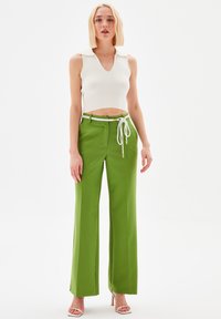 Pantaloni ampi verdi con vita a coulisse bianca e dettagli in metallo argentato, abbinati a un top corto a maniche corte con scollatura a V bianco a coste.