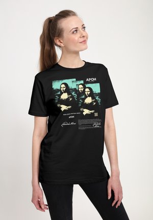 Kvinde med langt hår bærer en sort T-shirt med tre styliserede Mona Lisa-billeder og tekst på en lys baggrund.
