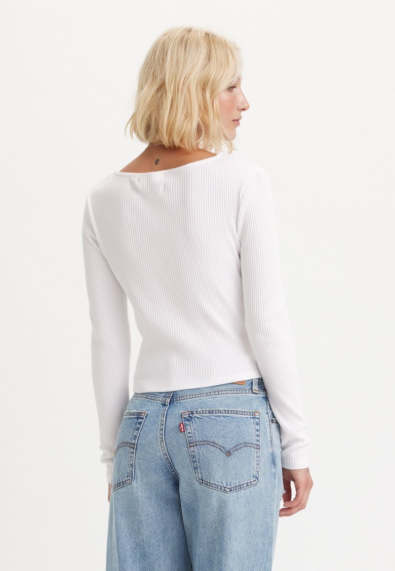 Maglietta bianca a coste con maniche lunghe e scollatura rotonda sul retro, abbinata a jeans azzurri a vita alta con dettagli di cucitura delle tasche in stile classico.