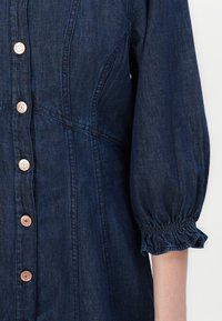 Jeansklänning med en figurnära bodice, puffärm och knappar i kopparfärg. Mörkblå tvätt med subtil textur och tydlig sömnad.