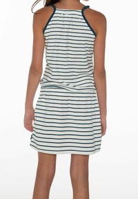 Dziecko w bezrękawnikowej białej sukience w granatowe poziome paski, widziane od tyłu na jednolitym białym tle.