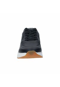 Zapato deportivo negro con parte superior texturizada y cordones planos, que presenta una entresuela blanca y una suela marrón, diseñado para comodidad y soporte.