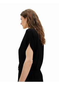 Schwarzes Kleid mit entspannter Silhouette, kurzen Dolmanärmeln und geraffter Taille. Es verfügt über einen strukturierten Stoff und einen subtilen Glanz.