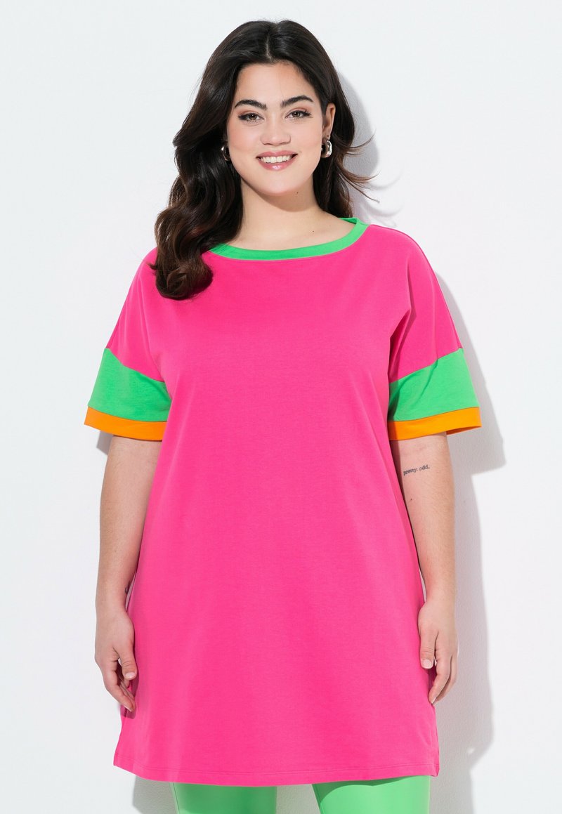 T-shirt oversize rose avec des accents verts et oranges sur les manches. Texture lisse, encolure ronde et coupe décontractée.