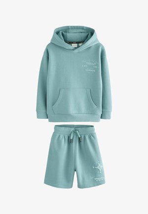 Gaiši tirkīza krāsas kapuce ar šortiem, izgatavota no kokvilnas materiāla, ar priekšējo kabatu, auklu jostasvīru un apdrukāta teksta un kompass dizaina detaļām.