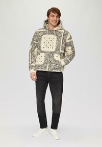 Sweat-shirt à capuche crème avec un motif floral noir, doté d'une poche frontale. Assorti avec un jean noir et des baskets blanches.