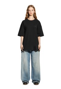 Czarna, oversize t-shirt z krótkim rękawem, zestawiona z jasnoniebieskimi, szerokimi dżinsami. Stylizacja zawiera prosty logo na koszulce.