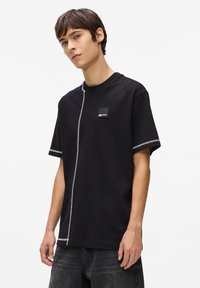 Tricou negru cu mâneci scurte, având un detaliu pe lateral evidențiat prin o cusătură albă și un mic buzunar pătrat pe piept.