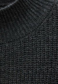 Gros plan sur un tissu tricoté gris foncé avec des motifs côtelés et texturés montrant les fibres de laine et les coutures détaillées.