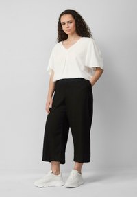 Witte V-hals blouse met korte, brede mouwen, gecombineerd met zwarte, cropped, losse broeken en witte sneakers. Eenvoudig en casual ontwerp.