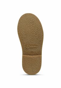 Hnědá gumová stélka s texturovaným povrchem a vyvýšeným logem, má oválný tvar s zaoblenými hranami.