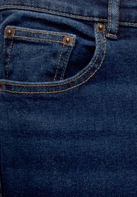Gros plan sur la poche d'un jean en denim bleu foncé avec des rivets en cuivre et des détails de couture contrastants orange.