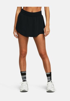 Femme portant un skort sportif noir, des chaussettes hautes noires et grises, et des baskets blanches, debout sur un fond blanc uni.