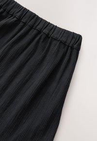 Czarna spódnica z elastycznym paskiem w talii i teksturowanym, prążkowanym wzorem. Materiał wydaje się lekki i zwiewny.