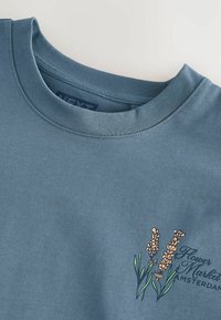 Blå bomulds sweatshirts med rund hals og broderet blomsterdesign i orange og grøn på forsiden. Letvægts stof.