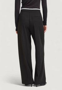 Pantaloni neri a gamba larga con una cintura elastica bianca e un dettaglio sulla tasca posteriore, realizzati in un tessuto liscio e strutturato.