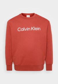 Červená mikina vyrobená z mäkkého materiálu s okr�úhlym výstrihom, s veľkým bielym logom "Calvin Klein" naprieč hrudníkom a pružnými manžetami.