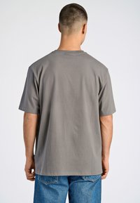 Camiseta de algodón gris con mangas cortas, corte relajado y cuello redondo. La tela tiene una textura suave sin patrones visibles.