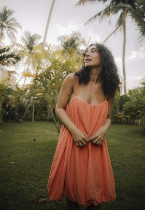 Koralowa sukienka bez rękawów o luźnym, zwiewnym kroju, z cienkimi ramiączkami i talią podkreśloną gumką. Miękka tkanina i strukturalny wzór zwiększają swobodę ruchów.