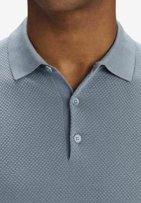 Ljusblå pikétröja i strukturerad väv, med krage, två knappar vid halsen och korta ärmar.