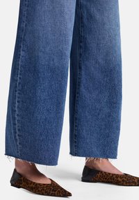 Jeans de mezclilla azul de pierna ancha con dobladillos deshilachados, combinados con zapatos planos de estampado de leopardo que tienen punta afilada y acentos negros.