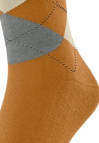 Calzino con un motivo argyle in marrone, grigio e crema, caratterizzato da linee cucite nere e una texture a coste su uno sfondo bianco.