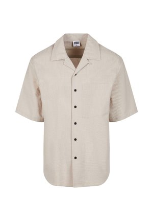Chemise beige à manches courtes texturée avec boutons noirs et poche poitrine, avec un large col.