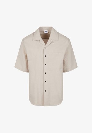 Chemise beige à manches courtes texturée avec boutons noirs et poche poitrine, avec un large col.