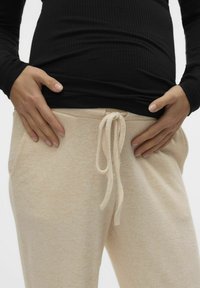 Beige sweatshirtbyxor med dragsko i midjan, med sidfickor och en mjuk, texturerad tyg. Kombinerad med en figurnära svart långärmad topp.