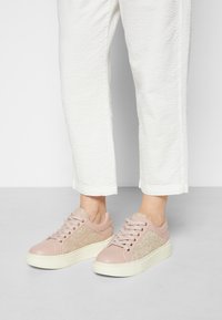 Rosa lädersneakers med sidopanel i snörmönster och en ljus gummisula, med snörningsdetaljer och rund tå.