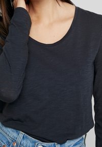 Långärmad, marinblå topp gjord av mjukt, lätt material. Har en rundad halsringning och subtil textur. Kombineras med högmidjade jeans.