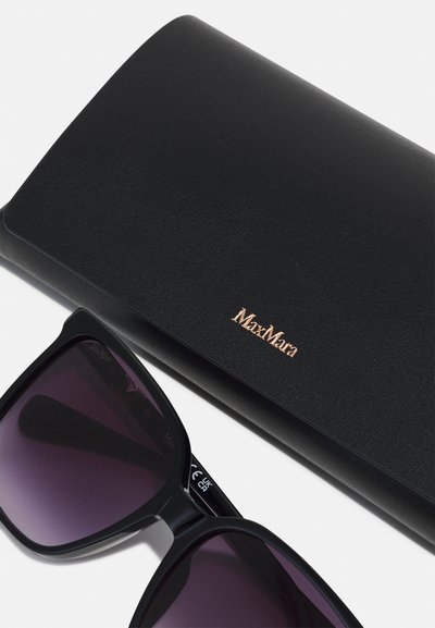 Óculos de sol pretos com uma armação quadrada, lentes roxas degradê e detalhes laterais. Acompanhados por uma elegante bolsa preta de pele com um logótipo dourado.