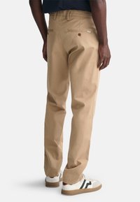 Pantalon kaki avec une texture lisse, une coupe droite et des poches arrière avec des boutons. Assorti à des baskets blanches avec des accents sombres.