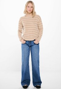 Beige randig stickad tröja med rundad hals, kombinerad med högmidjade blå jeans med utsvängd benmudd. Avslappnad passform, avslappnad design, strukturerad tyg.