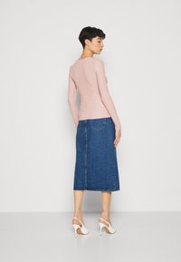 Rosa gerippter Langarmoberteil kombiniert mit einem hochgurten blauen Jeansrock. Weiße Sandalen mit offenen Zehen, Rückansicht, minimalistisches Design, ohne Muster.