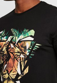 Camiseta de manga corta negra con un gráfico geométrico de un tigre adornado con follaje verde y acentos blancos, fabricada con material de algodón suave.