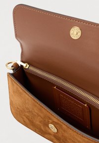 Καφέ πορτοφόλι από σουέτ και δέρμα με τσέπη με μεταλλικό φερμουάρ, χρυσαφένιες λεπτομέρειες και λογότυπο της μάρκας στο μπροστινό μέρος.