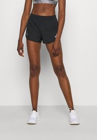 Svarta träningstights med elastiskt midjeband och vit Nike-logotyp. Matchat med vita träningsskor och en grå kortärmad topp.