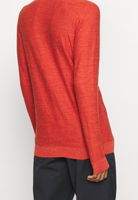 Pull rouge à manches longues en tissu tricoté texturé, avec une coupe décontractée, un ourlet arrondi et des poignets côtelés. Pas de motifs ou accents visibles.