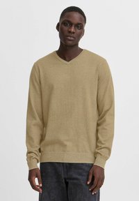 Lys beige, langermet genser med V-hals i strikket stoff. Ribbestrikkede mansjetter og nederkant, med et strukturert mønster over kroppen.