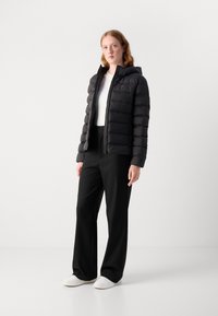 Black puffer jacket with a hood, quilted design, front zipper, worn over a white top, paired with black wide-leg pants and white sneakers.