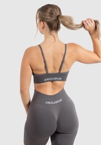 Grauer Sport-BH und hoch taillierte Leggings mit dem Markennamen "SMILODOX" in Weiß bedruckt. Glatte Textur, verstellbare Träger und figurbetontes Design.