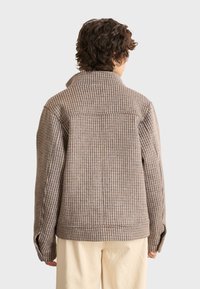 Brown and blue checkered jacket with a high collar, loose fit, and buttoned cuffs, made from woven fabric. Features a back yoke detail.