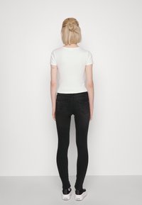 Vit kortärmad topp kombinerad med svarta skinny jeans. Outfiten har en figursydd design med enkla linjer och minimaliska detaljer, bärs med sneakers.