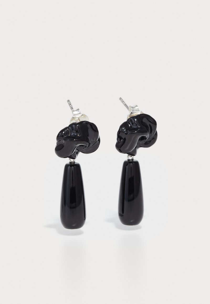 Schwarze Ohrringe mit einem einzigartigen skulpturalen Oberteil und einem verlängerten Tropfendesign. Glänzende Oberfläche mit Hardware in Silberoptik.