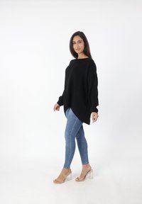 Zwarte oversized gebreide trui met lange mouwen, hoge lage zoom, gecombineerd met lichtblauwe skinny jeans en doorzichtige block-heeled sandaaltjes.
