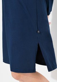 Mörkblå klänning med mjukt tyg, knälång design och detalj med slits på sidan. Inkluderar en liten etikett nära fållen.