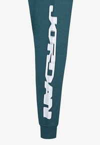 Mėlynos spalvos treningai su balta "JORDAN" užrašu vertikaliai palei kairę koją. Turi minkštą tekstūrą ir gumbuotus kulkšnių atvartus.